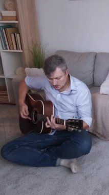 Dikey video. Gitar keyfi. İlham perisi. Sıradan bir adam yerde oturup akustik enstrüman çalıyor. Oturma odasının içinde, fotokopi odasının içinde en sevdiği melodi çalıyor..