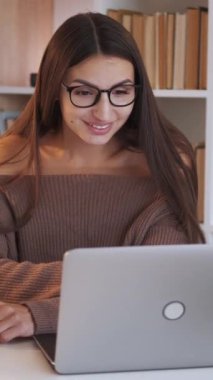 Dikey video. Çevrimiçi çağrı. Sanal toplantı. Gülümseyen kadın, masa başında oturmuş dizüstü bilgisayarla konuşuyor ve ev içi aydınlık internet bağlantısının keyfini çıkarıyor..