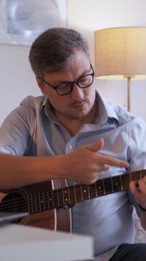 Dikey video. Gitar dersi. Müzik öğretmeni. İnternetteki konferans. Evde masadaki laptopta akustik enstrüman çalmayı açıklayan sıradan bir adamdan esinlendim..