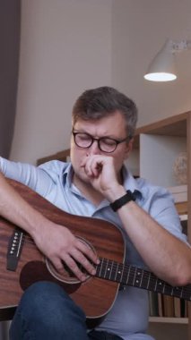 Dikey video. Gitar ilhamı. Düşünceli bir besteci. Enstrümanlı sıradan bir ozan. İç mekândaki ilham perisi ile kafası karışmış..