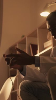 Dikey video. Doktor Leisure. Oyun hobisi. Gezici eğlence. Kulaklıklı sinsi, heyecanlı erkek doktor evde telefonla oynarken eğleniyor..