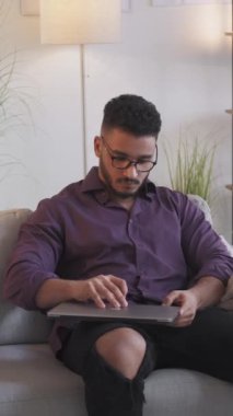 Dikey video. Uzaktan kumanda. Serbest bir iş. Modern ev oturma odasındaki koltukta dizüstü bilgisayar kullanan kendine güvenen zeki bir iş adamı..