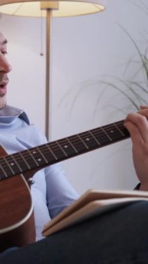 Dikey video. Yeni melodi. İlham verici gitarist. Beste hobisi. Duygusal adam akustik telli enstrüman çalıyor. Evde sesten hoşlanan akorların notalarını yazıyor..