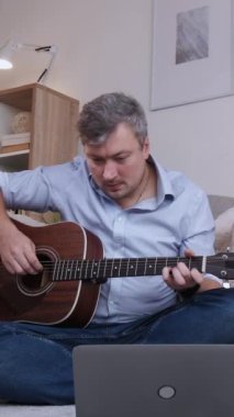Dikey video. Gitar öğrencisi. Sanal eğitim. İnternet müzik dersi. Melodi çalan mutlu, ilham verici adam evde dizüstü bilgisayar konferansında oturmuş başarının tadını çıkarıyor..