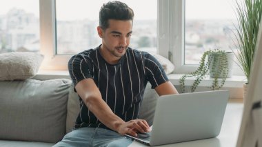 Mesafe çalışması. Bilgisayar teknolojisi. Odaklanmış serbest yazar dizüstü bilgisayarı kaydırıyor evdeki oturma odasındaki koltukta oturuyor..