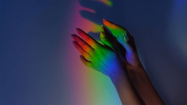 Gökkuşağı dokunuşu. LGBT renkleri. Eşitlik kültürü. Özgür aşk. Simgesel poz veren kadın elleri, fotokopi uzayının mavi gölgesi arkaplanında parlak ışık gradyanı ile bulanık neon renginde..