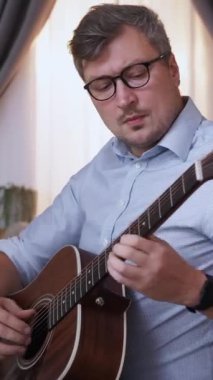 Dikey video. Gitar çalıyor. İlham verici bir müzisyen. Ev tatili. Odaklanmış akıllı adam melodi akorlarını eğitiyor. İçerideki telli çalgılar üzerinde yetenek kazanıyor..