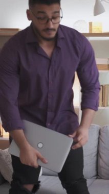 Dikey video. Online iş. Sanal iş. Dijital pazarlama. Modern ofis içlerinde kendine güveni olan akıllı bir adam kanepeye dizüstü bilgisayar kullanıyor..