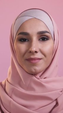 Dikey video. Mutlu Müslüman kadın. Pozitif tavır. Geleneksel kıyafet. Pembe stüdyo arka planında izole edilmiş tesettürlü neşeli kadın yüzü portresi.