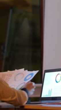 Dikey video. İş planlaması. Takım çalışması toplantısı. Erkek uzman beyaz tahtada başlangıç stratejisi yazıyor. Kadın ortak akşam ofisi ile mali istatistik belgelerini tartışıyor..