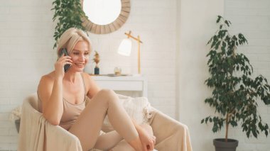 Telefon var. İletişim eğlencesi. Neşeli, mutlu, rahat kadın akıllı telefonuyla konuşuyor koltukta oturmuş fotokopi odasında hafta sonunun tadını çıkarıyor..