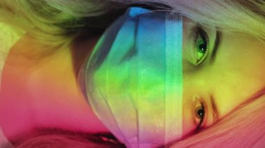 Dikey video. Pandemik tedavi. Hastalık önleme. Karantina yaşam tarzı. Kapsamlı terapi. Gökkuşağı ışığında koruyucu maskeli mutlu sarışın kadın portresi.