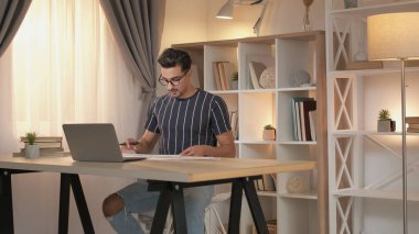 Mesafe çalışması. Rapor hazırlanıyor. Profesyonel bir adam, ofis içi fotokopi alanında dizüstü bilgisayarla masa başında iş evrakları üzerinde çalışıyor..