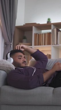 Dikey video. Hüzünlü müzik. Hafta sonu melankolisi. Dijital yalnızlık. Rahatlamış depresif adam kulaklıkla telefon dinleyen evde yalnız başına kanepede telefon kullanan..