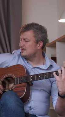 Dikey video. Melodi ilhamı. Enstrümantal performans. Gitar akorları çalan sıradan yetenekli müzisyen ev içinde neşe hissediyor..