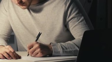 Gece çalışması. Sınav hazırlığı. Online eğitim. Yoğunlaştırılmış özenli öğrenci notlar alıyor. Geç saatlerde karanlık evde dizüstü bilgisayar kullanarak ders çalışıyor..