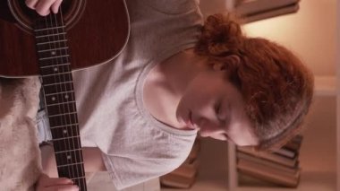 Dikey video. Müzik alıştırması. Gitar keyfi. Evde oturma odasındaki kanepede akustik bir enstrüman çalan müzisyen kızdan esinlendim..