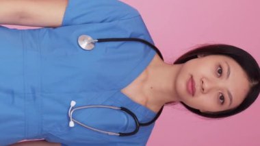Dikey video. Kadın sağlık görevlisi. Acil servis. Düşünceli, sakin, yorgun bayan hemşire mavi ışıklar altında dikiliyor. Acil ilaç pembe arka plan..
