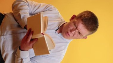 Dikey video. Eğitim süreci. Akıllı adammış. Şişman, şişman, gözlüklü adam. Kitapta ilginç bilgiler okuyor. Şaşırtıcı yüzü sarı arka planda izole edilmiş..