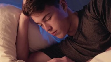 Yorgunluk okuyorum. Yorgun ve yorgun genç bir adam, gece yumuşak ışıkta kitap yatağıyla huzur içinde uyuyor..