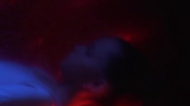 Dikey video. Çocuk koruma. Bulanık siluet. Endişeli kız yürüyor. Neon kırmızı ışıktaki strese bakıyor. Plastiğin odak noktasını kaybetmiş..