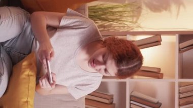 Dikey video. Telefon şakası. Oyun eğlencesi. Mobil cihazlı heyecanlı kadın video siber spor ev kanepede dinleniyor sıcak oturma odasında..