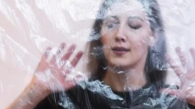 Plastik çarşafların arkasında kapana kısılmış bir kadın yalnızlığı simgeler. Gerçeküstü bir ortamda duygusal mücadele..