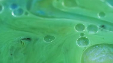 Parlayan yağ damlaları. Boya dökülmüş. Odaklanmamış yeşil renk akan parlak mürekkep parçacıkları yüzen parlak su kabarcıkları parlak sıvı akış hareketi soyut sanat arka planı.