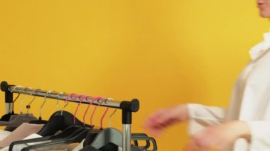 Alışverişkolik yaşam tarzı. Kişisel stil. Tatmin olmuş olgun bir kadın sarı arka planda izole görünmek için askılarda bluz seçiyor..