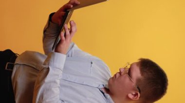 Dikey video. Serbest bir iş. Programlama öğreniyorum. İnternet iletişimi. Çevrimiçi yoğunluğu sarı üzerine izole edilmiş dizüstü bilgisayar kullanan dalgın şişman bir adam..