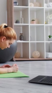 Dikey video. Çevrimiçi antrenman. Denge egzersizi. Fitness eğitimi. Spor müsabakası. Aktif giyimli formalı bir kadın hafif ev içi dizüstü bilgisayarla yoga minderinde kalas yapıyor..