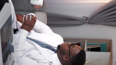 Dikey video. Doktorlar rahatlar. İş molası. Tıbbi ekip. Konuşan adam ve kadın pratisyen doktor hastanedeki kanepede bir fincan kahveyle sohbet ediyor..