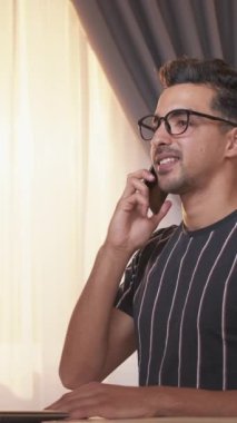 Dikey video. Telefon görüşmesi. Mobil iletişim. Yakışıklı, sıradan gülümseyen adam akıllı telefondan evdeki önemli bilgiler hakkında konuşuyor..