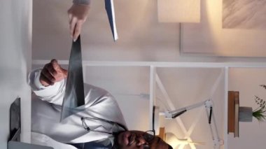 Dikey video. Doktor ekip çalışması. Radyoloji teşhisi. Profesyonel sağlık hizmeti. Dizüstü bilgisayardaki erkek doktor klinikteki üniformalı kadın hemşireyle röntgen taramasını onaylıyor..