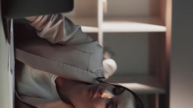 Dikey video. Uykucu işçi. Aşırı çalışma yorgunluğu. Uzun çalışma saatlerinden sonra bilgisayarını kapatmak için esnemekten yorgun düşmüş bir kadın geç kaldı..
