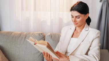 Dinlenme işi. Mutlu kadın. Başarılı bir yaşam tarzı. Şık gülümseyen bayan kanepede oturmuş, aydınlık odada ilginç kitaplar okuyor..
