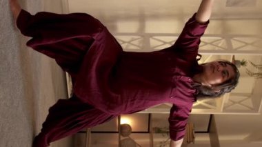 Dikey video. Yoga esneme hareketleri. Sağlıklı aktivite. Kapalı alanda eğitim. Virabhadrasana savaş güvercini pozu veren motive olmuş bir kadın. Evdeki refahın tadını çıkarıyor..