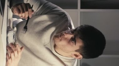 Dikey video. Geç yemek. Laptop rahatla. Akşam yemeği. Ciddi şekilde konsantre olmuş erkek serbest çalışan yemek yiyor, dinleniyor, işten sonra film seyrediyor, karanlık ev ofisinde..