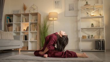 Yoga esneme hareketleri. Esneklik egzersizi. Aktif hobi. Dikkatli kadın bacak egzersizi yapıyor. İdman güvercini pozu veriyor. Oturma odasında eğiliyor..