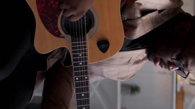 Dikey video. Gitar müziği. Sanatçı oynuyor. Şarkı söyleme alıştırması. Yetenekli bir adam akustik telden caz melodisini öğreniyor..