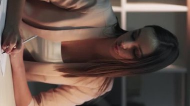 Dikey video. Ev ödevi. Çevrimiçi öğrenme. İş yerindeki sakin iş kadını el yazısı notları ve dizüstü bilgisayar sınavı hazırlığı.