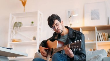 Guitar hobby. Music playing. Creative skill. Rock weekend. Inspired man tuning up acoustic instrument strings checking sound at light modern home interior with free space. clipart