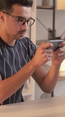 Dikey video. Mobil oyunlar. Gadget bağımlılığı. Dijital eğlence. Modern iç mekanlarda masa başında oturmuş akıllı telefondan keyif alan sıradan bir adam..