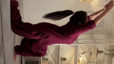 Dikey video. Yoga çalışıyorum. Ev jimnastiği. İyi bir eğitim. Anjaneyasana 'da esnek, barışçıl bir esneme hareketi yapan kadın oturma odasında hafif bir hareket sergiliyor..