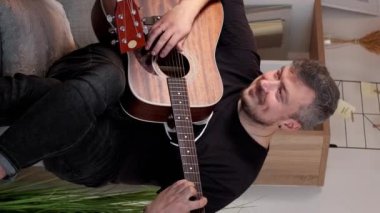 Dikey video. Gitar alıştırması. Düet çalıyor. Müzik provası. Neşeli erkek arkadaşlar evdeki kanepede birlikte şarkı söylüyor..