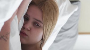 Dikey video. Uykulu bir sabah. Sinir bozucu alarm. Erken yorgunluk. Depresyondaki kızın uyanması kafası karışık. Yatak odasındaki telefona bakmaktan yorgun düşmüş..