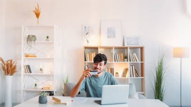 Çevrimiçi bankacılık. İnternet ödemesi. Elektronik işlem. Doymuş gülümseyen adam, açık modern ev işyerinde kredi kartı bilgisayarı kullanıyor..