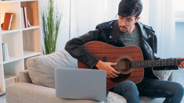 Online gitar dersi. Müzik dersi. Yaratıcı hobi. Yetenekli müzisyen, akustik enstrüman çalmayı öğreniyor. Ev içinde boş alan olan dizüstü bilgisayarda video dersi izliyor..