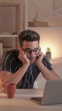 Dikey video. Sıkıcı iş. Bağımsız çalışmaktan yoruldum. Sanal bağlantı. Laptop iş uzak konferansında uykulu adam oturma odasının iç kısmında oturuyor..