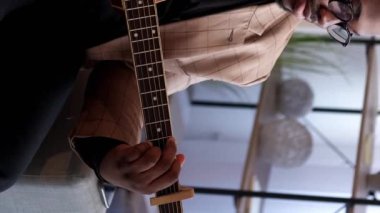 Dikey video. Erkek gitarist. Müzikal eğlence. Melodi çalışması. Yetenekli, tatmin olmuş erkek sanatçı evde akustik enstrüman ile şarkı akorları çalıyor..